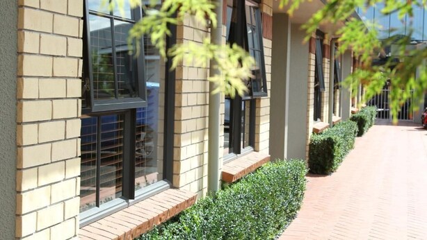 Un edificio con fachada de ladrillo, ventanas amplias y un camino de ladrillo con setos podados.
