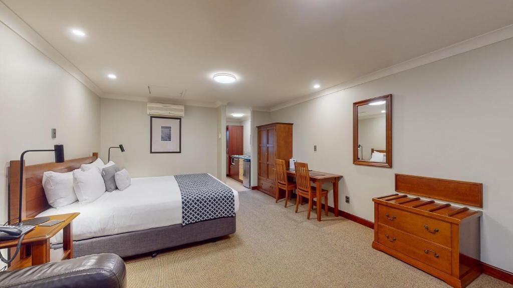 Habitación de hotel con cama, escritorio, silla, cómoda y espejo.