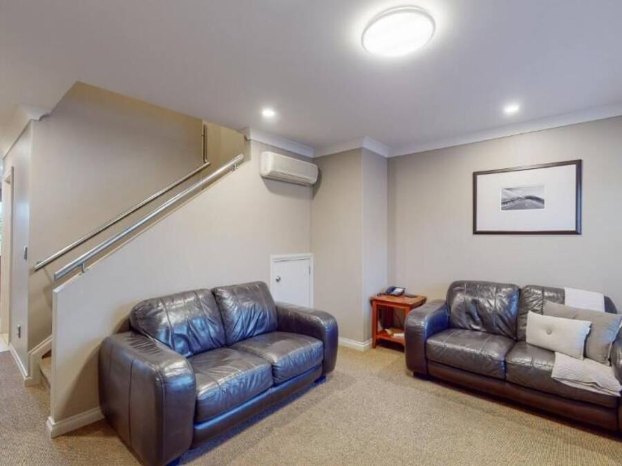 A living room with two leather sofas, a staircase, a framed picture on the wall, and a small side table.