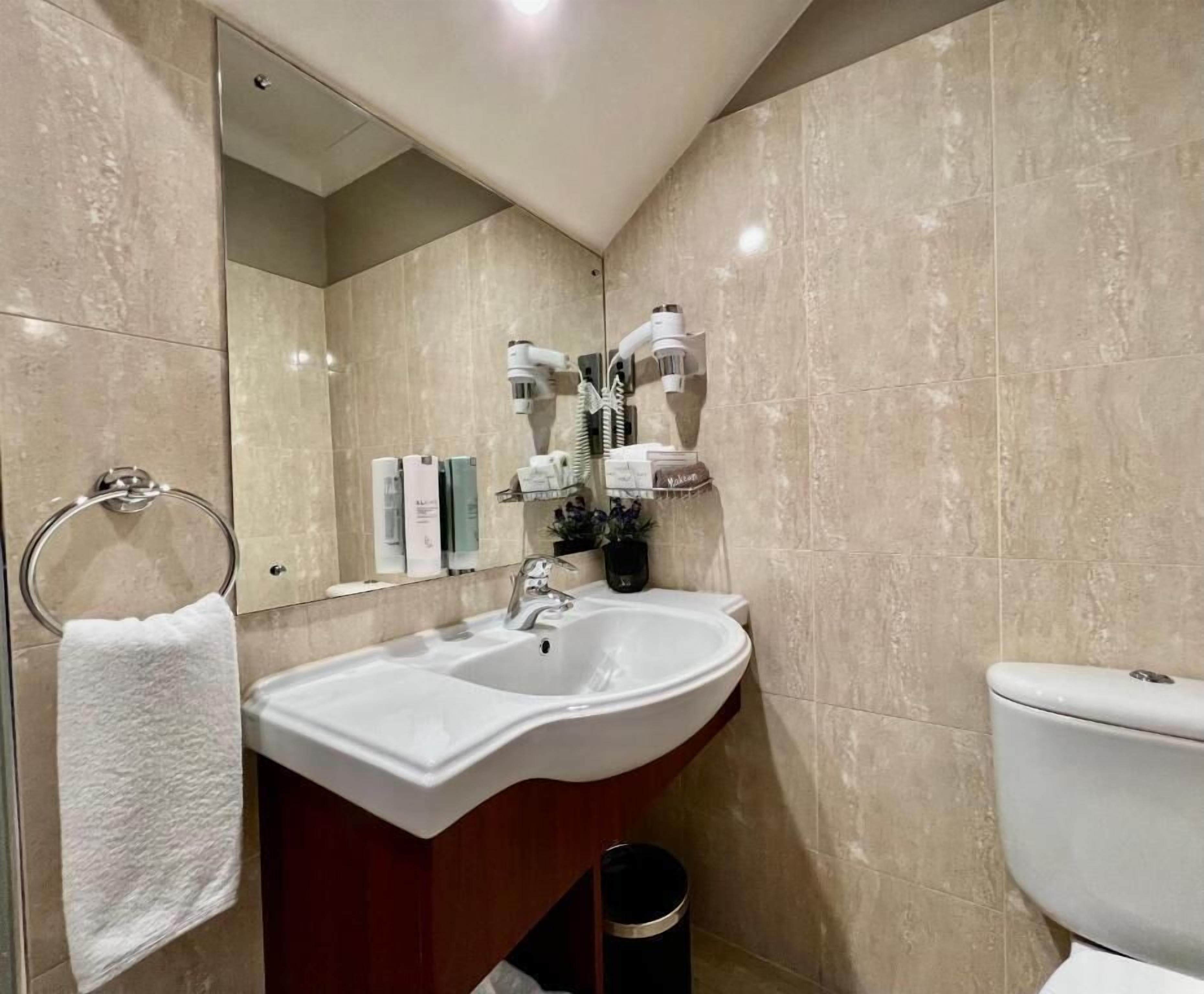 A bathroom with a white sink, a mirror, and a toilet. There are toiletries on the sink and a towel hanging on the wall.