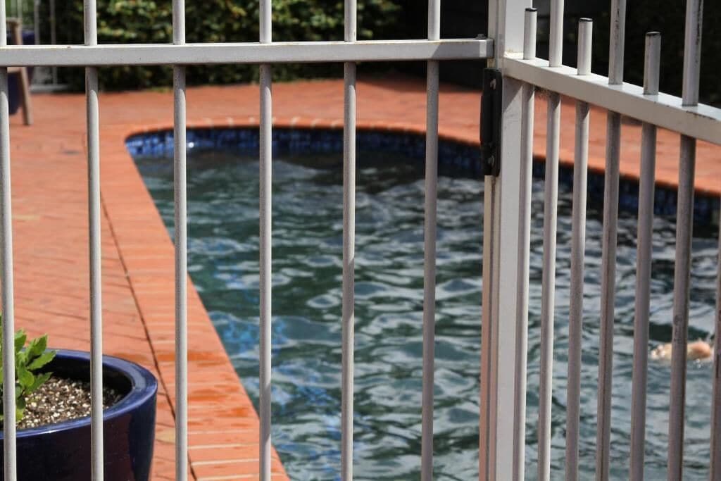 A pool area with a tiled deck and a metal fence.