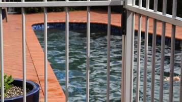 A pool area with a tiled deck and a metal fence.
