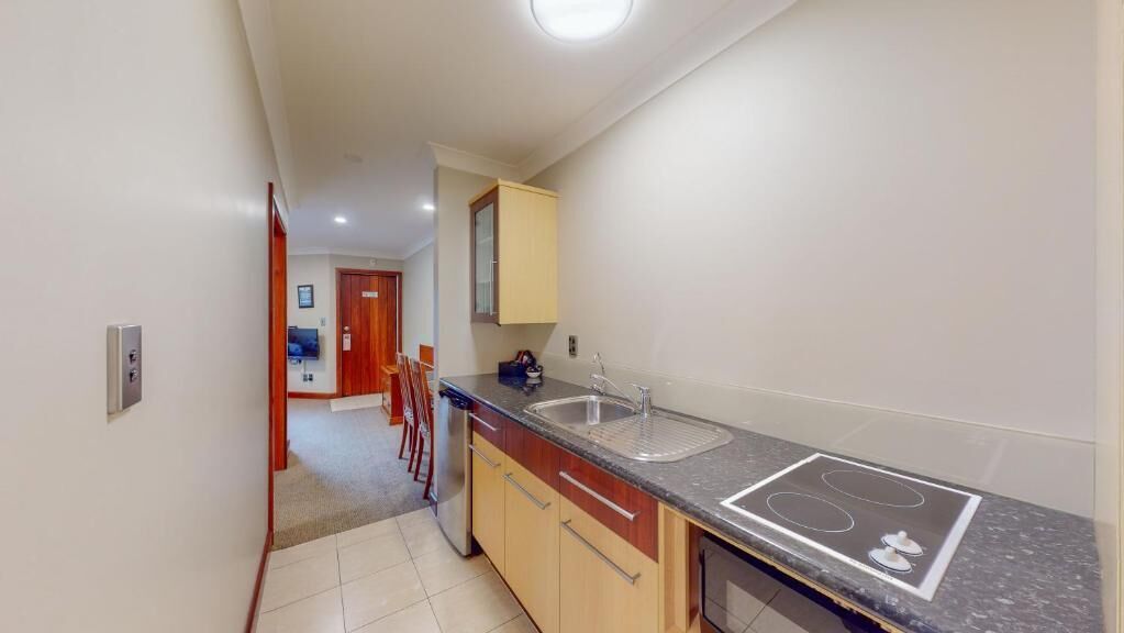 A narrow kitchen with a stove, sink, and wooden cabinets.