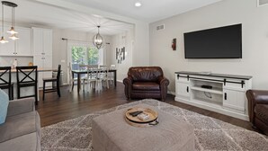 A spacious living room with a large flat-screen TV, a leather armchair, and a dining area with a chandelier.