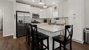 A modern kitchen with white cabinets, stainless steel appliances, and a granite island with bar stools.