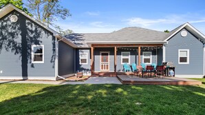 A two-story house with a covered porch, a dining area with outdoor furniture, and a well-maintained lawn.