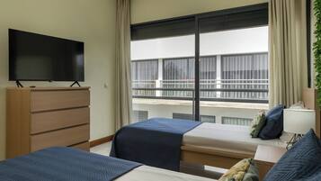 Ein Hotelzimmer mit Fernseher auf einer Holzkommode, zwei Betten mit blauer Bettwäsche, einem großen Fenster mit Blick auf Gebäude und einer Pflanze auf der rechten Seite.