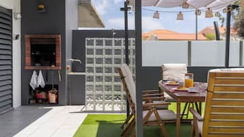 Eine Terrasse im Freien mit Esstisch, Stühlen und Grillplatz.