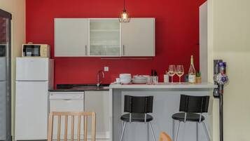 Una cucina compatta con una parete rossa, mobili bianchi, un forno a microonde, un lavandino e un angolo ristoro con due sedie.