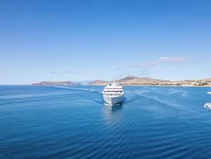 Ein Kreuzfahrtschiff auf ruhiger See unter einem wolkenlosen Himmel, in der Ferne Land.