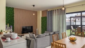 A modern living room with a flat-screen TV, grey sofa, dining table with chairs, and a balcony with a view. - Vacation home in Porto Santo, Villa Girassol (Porto Santo)