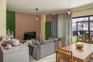 A modern living room with a flat-screen TV, grey sofa, dining table with chairs, and a balcony with a view. - Vacation home in Porto Santo, Villa Girassol (Porto Santo)