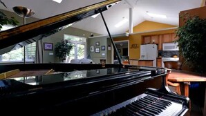 A grand piano in a room with a kitchen area visible in the background. - Amazing Home...Large Space Yet Cozy (Kirkland)
