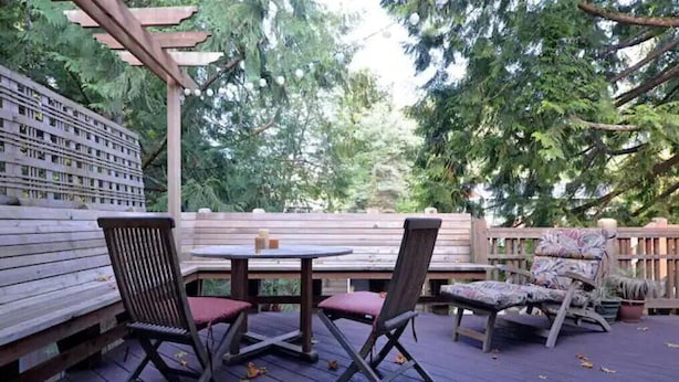 An outdoor deck with a wooden table and two chairs, surrounded by a wooden fence and trees. - Amazing Home...Large Space Yet Cozy (Kirkland)