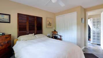 A bedroom with a bed, wooden headboard, a ceiling fan, a dresser, a chair, a door, and a window.