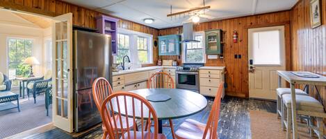 A kitchen with wooden paneling, a refrigerator, a stove, and a dining area with chairs and a table.