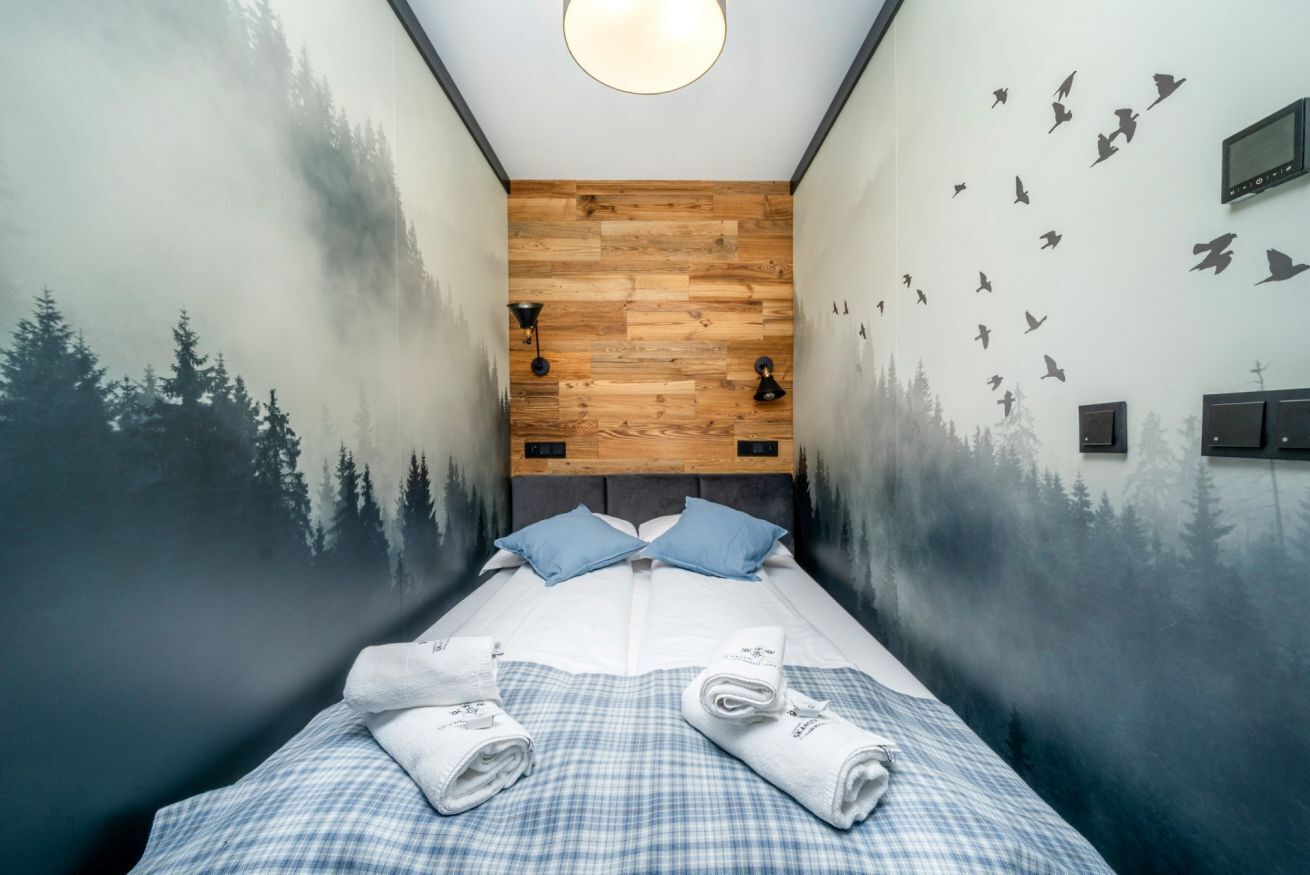 A bedroom with a bed, two pillows, a checkered bedspread, a wooden headboard, wall art, and a ceiling light.