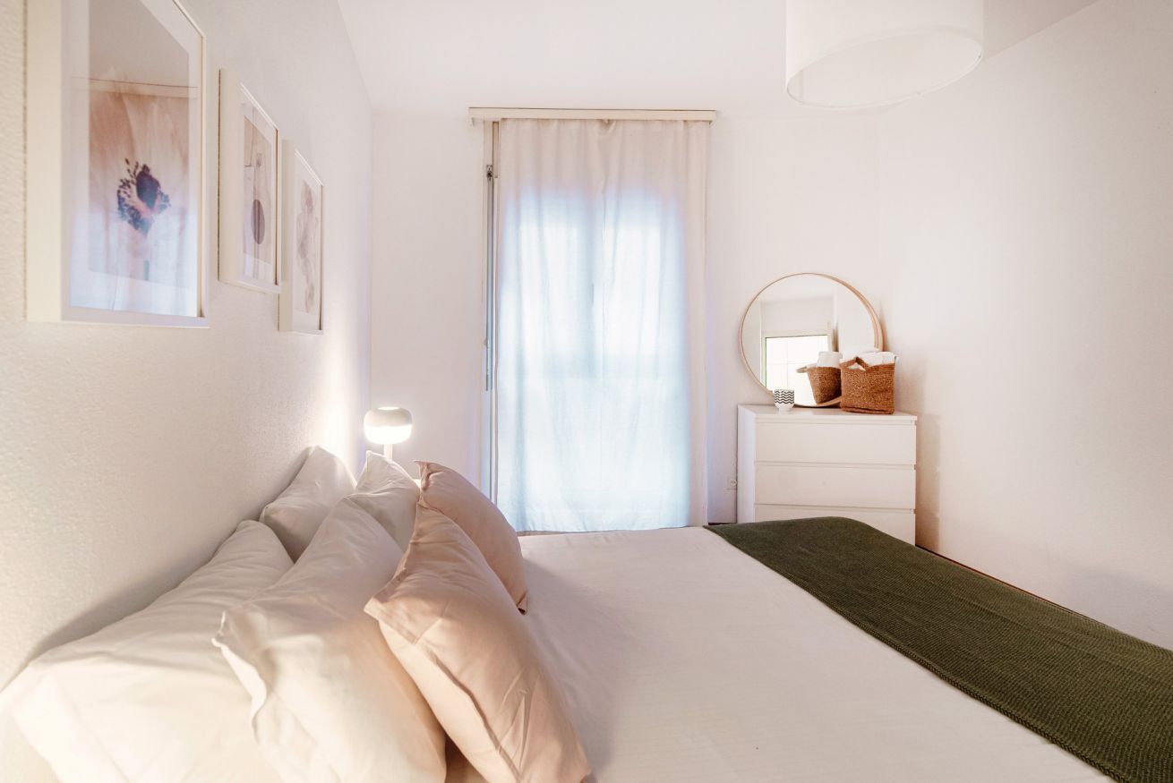 Una camera da letto con un letto, una cassettiera, uno specchio e una finestra con tende.