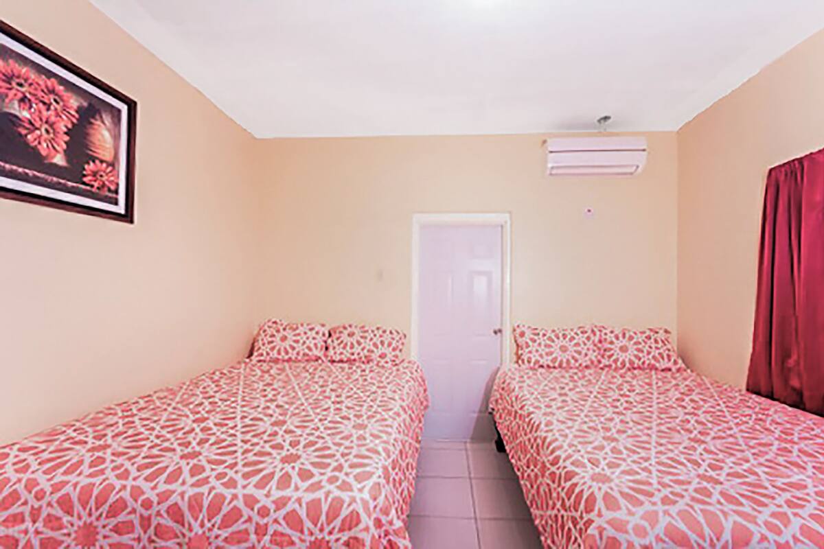 Een kamer met twee bedden, beige wanden, een deur en een airconditioner.