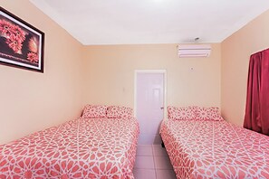 A room with two beds, beige walls, a door, and an air conditioning unit. - Scarlett Guesthouse By The Sea (Bull Bay)