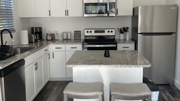 A modern kitchen with white cabinets, stainless steel appliances, a granite countertop, and a central island with bar stools. - Cozy Guest House located near downtown! 







































 (Hickory)