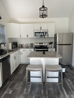Een moderne keuken met witte kasten, roestvrijstalen apparatuur, een granieten werkblad en een centraal eiland met barstoelen.