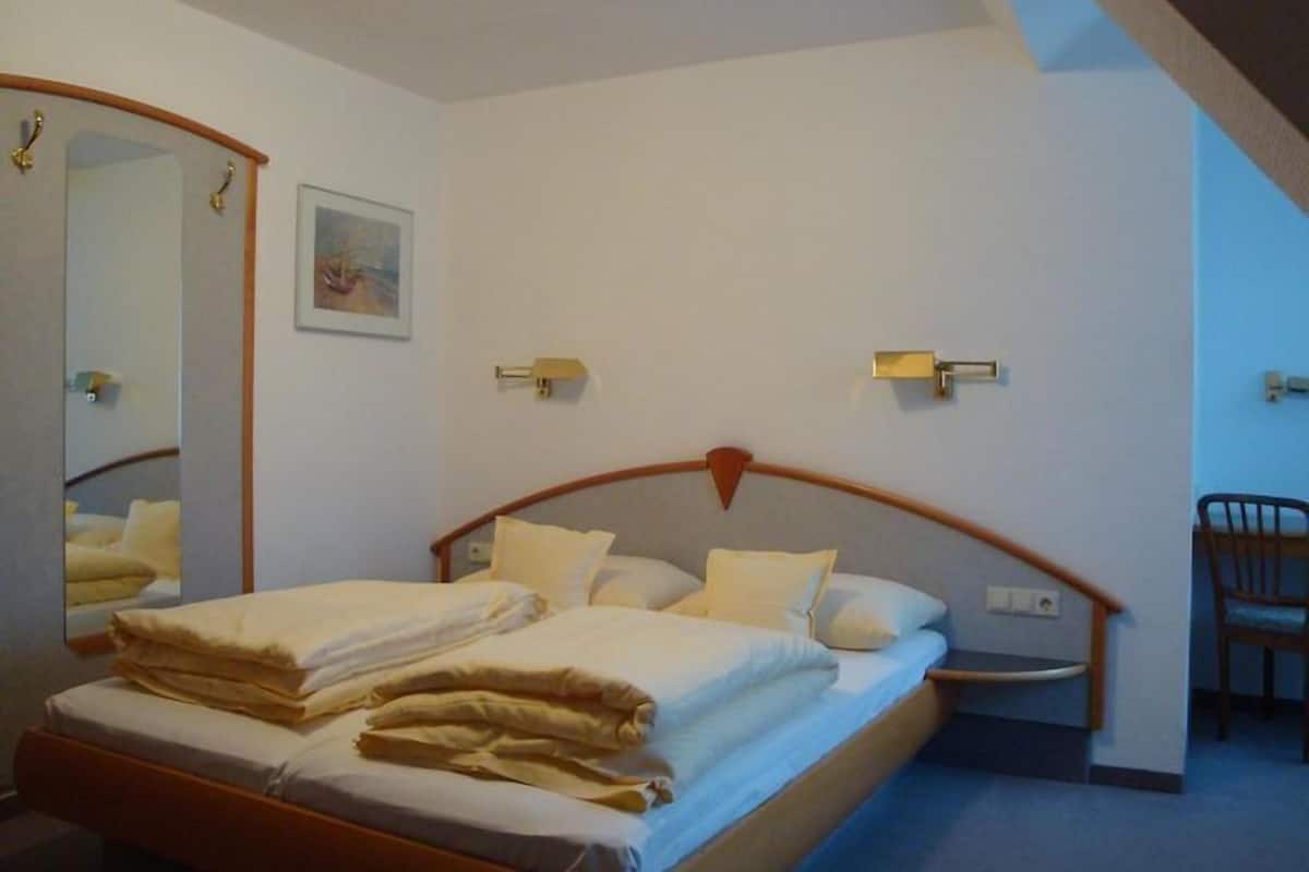 A bedroom with a bed, a chair, a mirror, and a wall-mounted light fixture.
