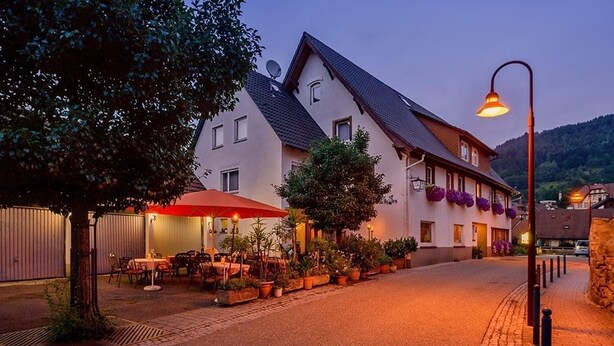 A building with a sloped roof and multiple windows, surrounded by potted plants and outdoor seating. - landgasthaus waldhorn (Forbach)