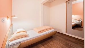 A small, neatly arranged bedroom with a single bed, a wooden floor, a mirror, and a wall-mounted light fixture. - landgasthaus waldhorn (Forbach)
