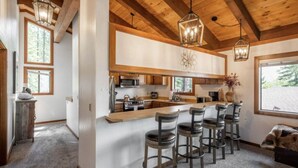 A modern kitchen with a central island, bar stools, and wooden ceiling beams.