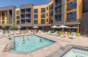 A modern building with a swimming pool, lounge chairs, and umbrellas. - Canyon Haus 301 - Mountainside Modern Deluxe Studio - Pool+Gym+Arcade (Park City)