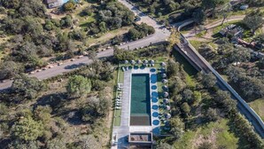 An aerial view of a resort with a swimming pool, lounge chairs, and a parking area surrounded by trees.