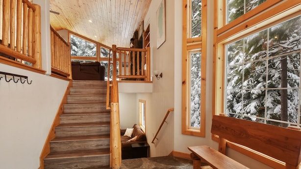 A wooden staircase with a stone floor leading to a second level. There is a bench and a window with a view of snow-covered trees.