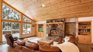 A cozy living room with a stone fireplace, leather sofa, and large windows overlooking a snowy deck.