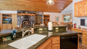 A kitchen with a stone fireplace, wooden cabinets, granite countertops, and a dishwasher.