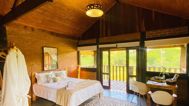 A spacious bedroom with a large bed, a desk, and a chair. There is a window providing a view of the outdoors.