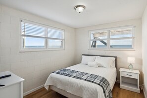 A bedroom with a bed, two nightstands, a lamp, and a window with a view of the sea. - 3 Little Pirates! Discounted Monthly Rate! Direct beach access, Private Oceanfront Deck (Folly Beach)