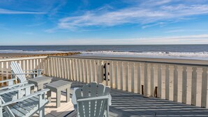 Een houten terras met witte Adirondack-stoelen en een tafel met uitzicht op het strand.