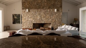 A modern living room with a stone fireplace, a sofa, a coffee table, and a dining area with a marble table. - Vista Deslumbrante e Alto Padrão com 4 Suites, Piscina Aquecida e Sauna (Santo Antônio do Pinhal)