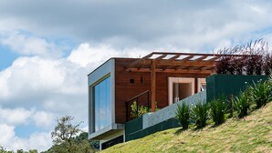 A modern house with a wooden exterior, a large window, and a green wall. - Vista Deslumbrante e Alto Padrão com 4 Suites, Piscina Aquecida e Sauna (Santo Antônio do Pinhal)