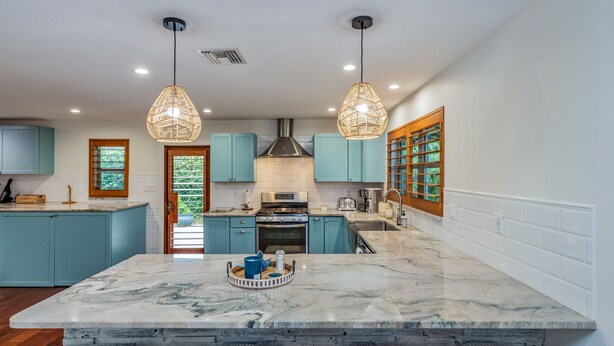 A modern kitchen with teal cabinets, a marble island, and pendant lighting.