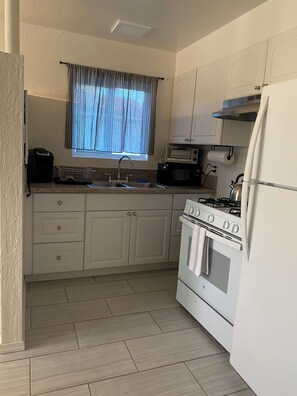 Una cocina con estufa, horno, microondas y una ventana con cortinas.