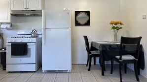 A compact kitchen with white appliances, a dining table with chairs, and a vase with flowers on the wall. - CocoVillaSB Apartment #4 (Santa Barbara)
