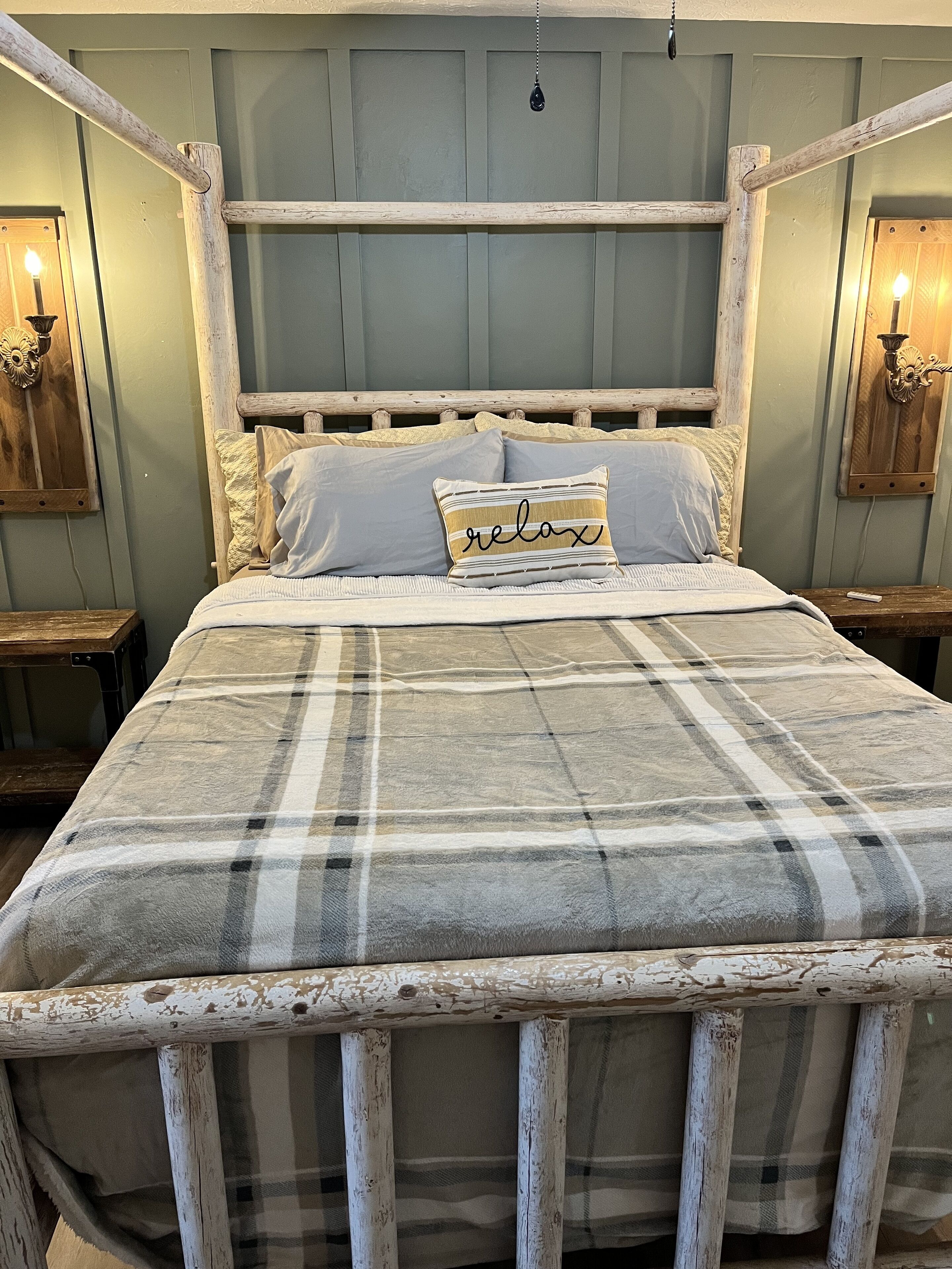 A bed with a plaid blanket, a pillow with the word "relax," and a wooden headboard.
