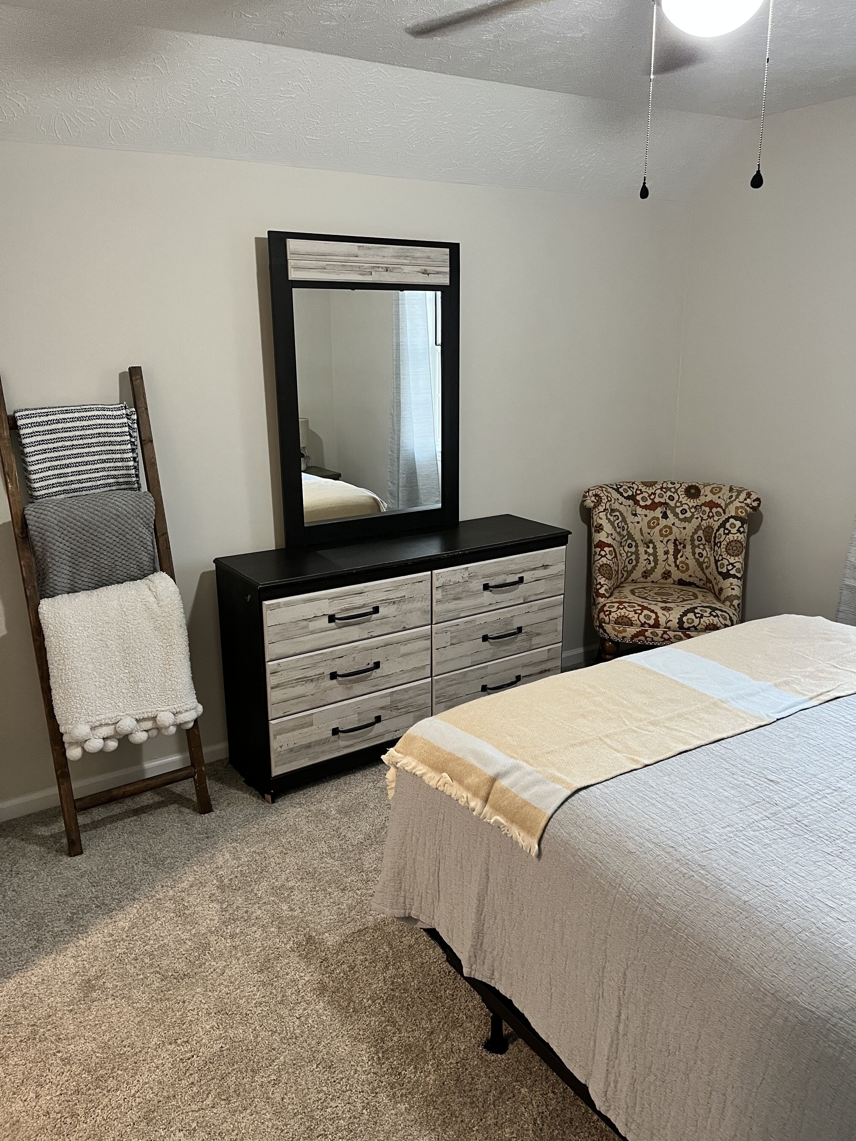 Une chambre à coucher avec un lit, une commode, une chaise et un miroir.