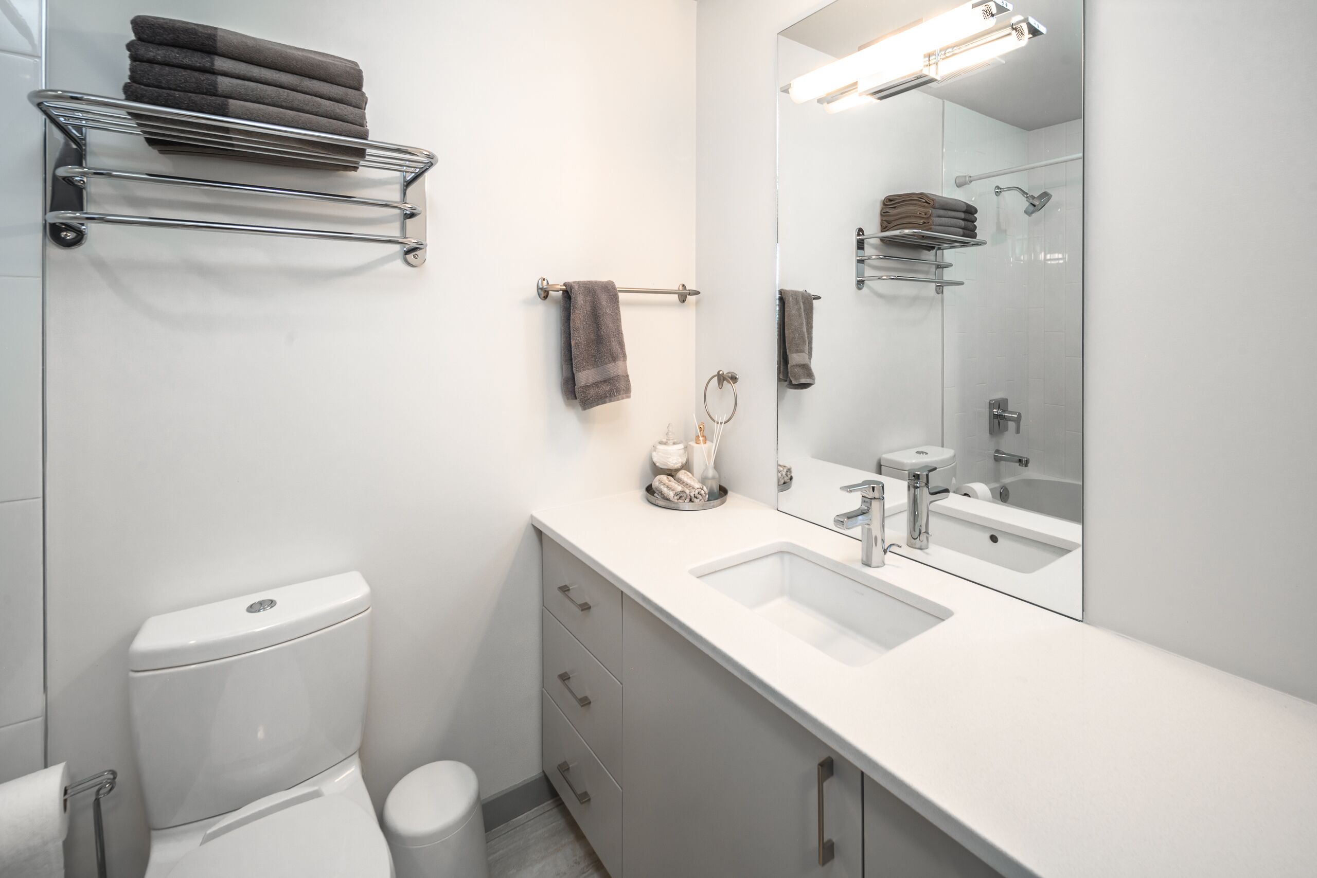 Un baño moderno con un lavamanos blanco, un espejo y un perchero para toallas.