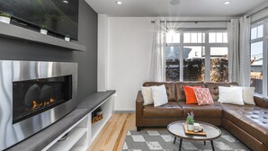 A modern living room with a fireplace, leather sofa, and a large window with curtains. - Detached, Luxury, mins to DT & Walking distance to C-train! (Calgary)