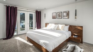 A modern bedroom with a large bed, a wooden headboard, and a glass door leading to a balcony. - Detached, Luxury, mins to DT & Walking distance to C-train! (Calgary)