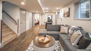 A modern living room with a grey sofa, a coffee table with a tray, and a staircase leading to another room. - Detached, Luxury, mins to DT & Walking distance to C-train! (Calgary)