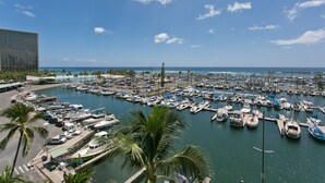 A marina with numerous boats docked, a clear blue sky, and a modern building in the background. - Renovated Oceanfront Condo (Honolulu)